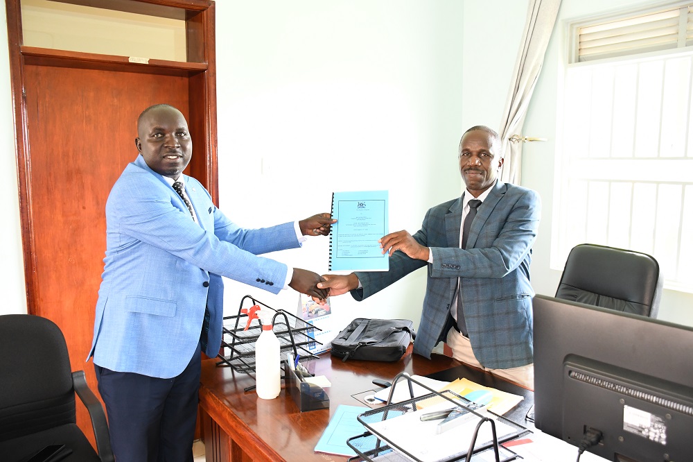 Outgoing Kiryandongo Deputy CAO Deo Kabugo (R) hands over office instruments to Principal Assistant CAO Denis Dacan during a ceremony at the district headquarters.